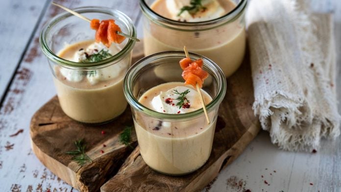 3 Gläser mit Cremesuppe vom Räucherlachs stehen auf einem Holzbrett