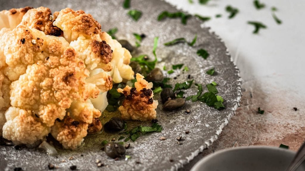 Ganzer Blumenkohl auf einem Teller mit Kapern Vinaigrette