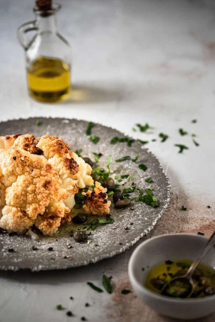 Ganzer Blumenkohl im Ofen mit Kapern auf Teller angerichtet