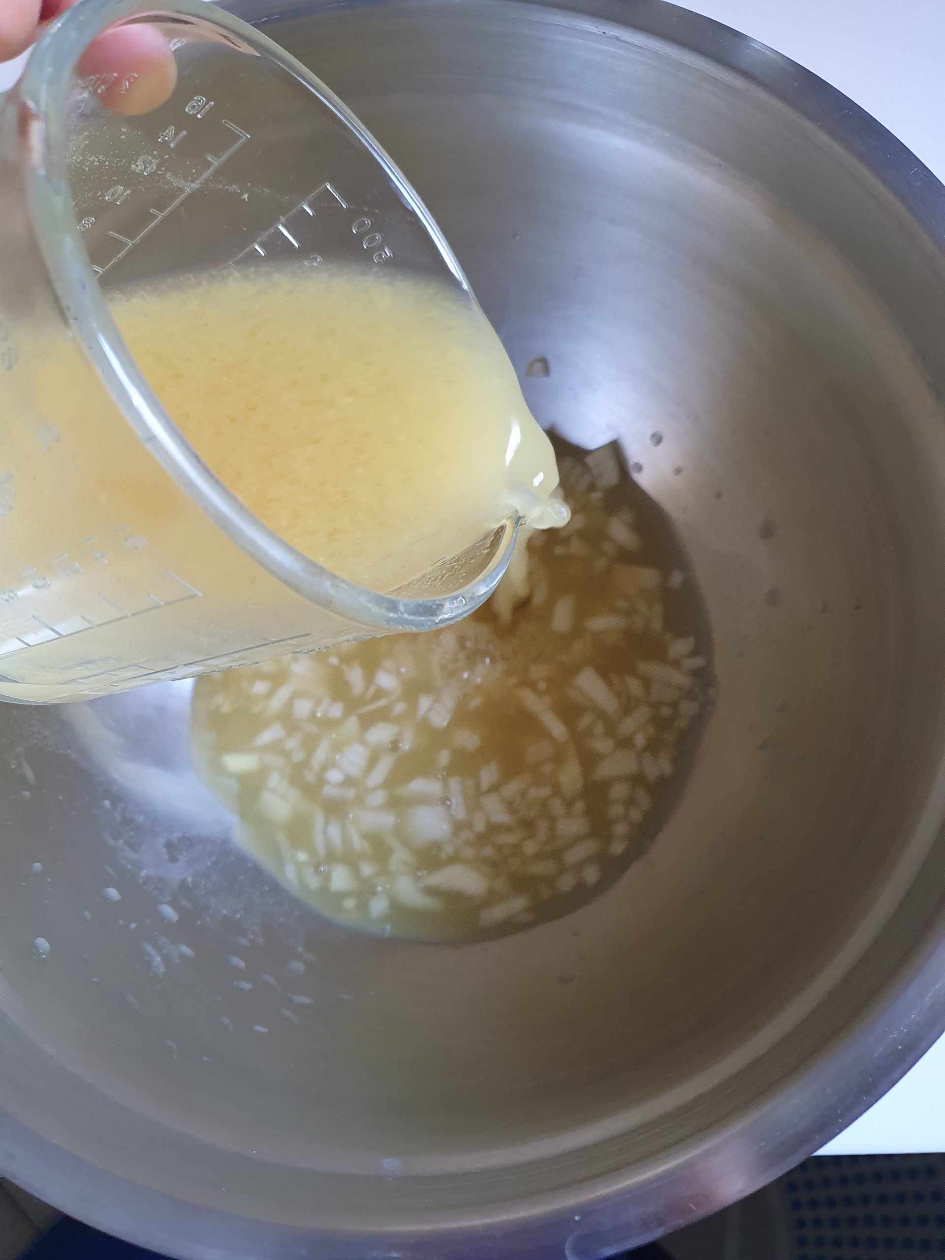 Marinade für Kartoffelsalat wird in Schüssel mit Zwiebeln geschüttet.