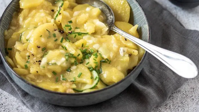 klassischer-kartoffelsalat-mit-essig-und-oel Eine Schüssel Kartoffelsalat steht auf Steinuntergrund.