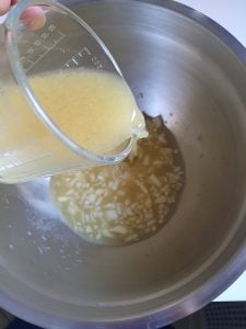 Marinade für Kartoffelsalat wird in Schüssel mit Zwiebeln geschüttet.