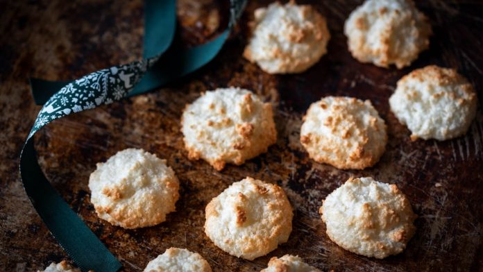 weiche-kokosmakronen-schnell-und-einfach Kokosmakronen liegen auf einem alten Backblech neben einer Schleife