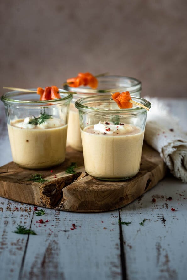 3 Gläser mit Cremesuppe vom Räucherlachs stehen auf einem Holzbrett