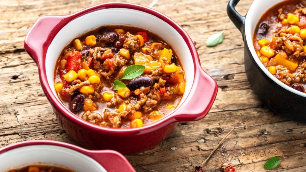 Drei Schälchen mit Chili con Carne stehen auf Holztisch