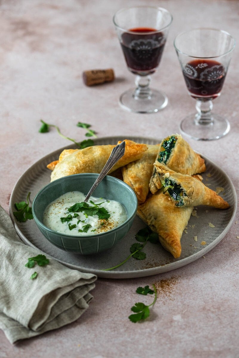Gefüllte Blätterteigtaschen liegen auf einem Teller und 2 Weingläser stehen daneben