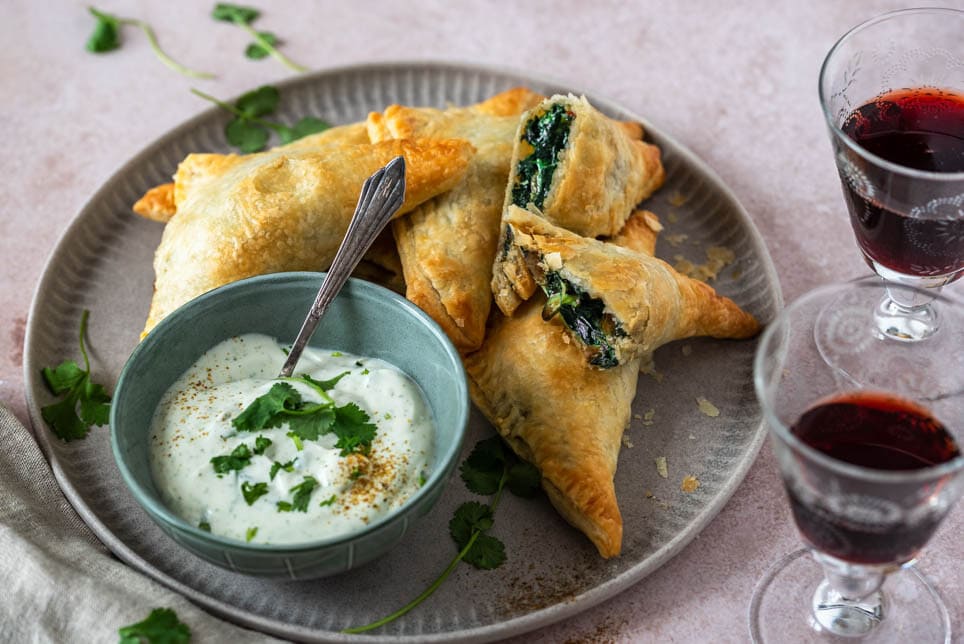 Gefüllte Blätterteigtaschen liegen auf einem Teller und 2 Weingläser stehen daneben