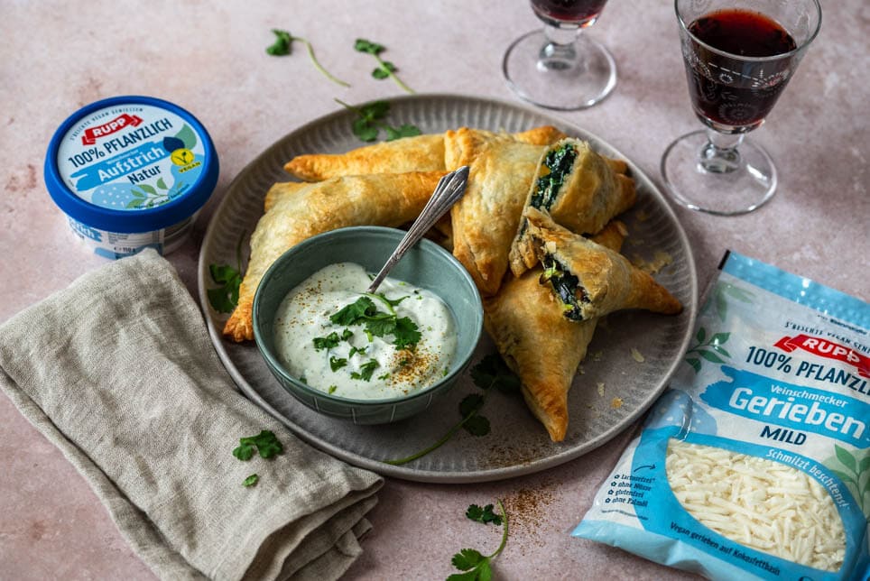 Gefüllte Blätterteigtaschen liegen auf einem Teller und 2 Weingläser stehen daneben