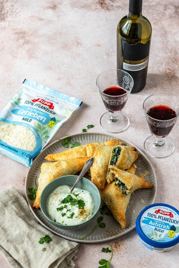 Gefüllte Blätterteigtaschen liegen auf einem Teller und 2 Weingläser stehen daneben