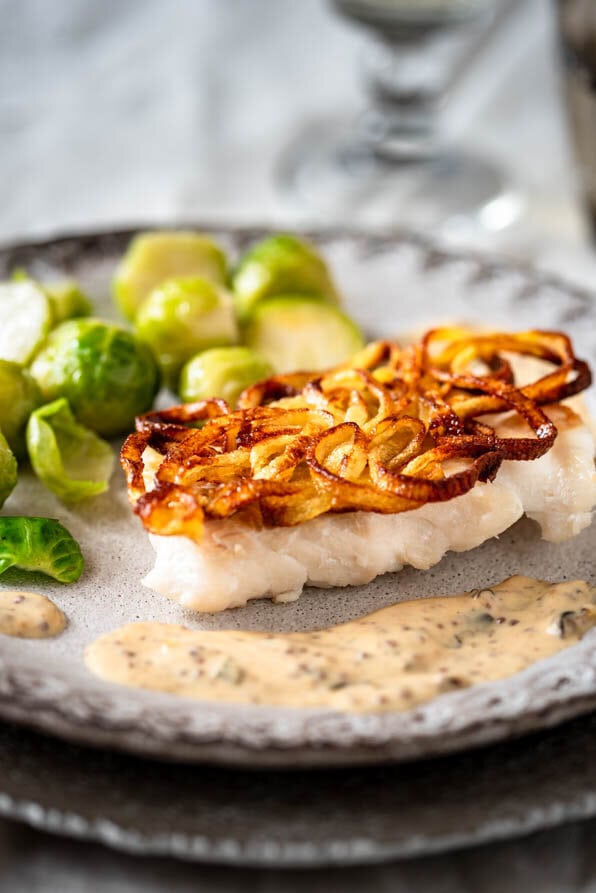 Kabeljau in der Kartoffelkruste mit Senfsauce und Rosenkohl auf gedecktem Tisch