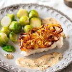 Kabeljau in der Kartoffelkruste mit Senfsauce und Rosenkohl auf gedecktem Tisch