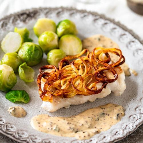 Kabeljau in der Kartoffelkruste mit Senfsauce und Rosenkohl auf gedecktem Tisch