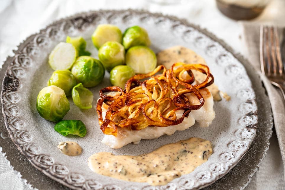 Kabeljau in der Kartoffelkruste mit Senfsauce und Rosenkohl auf gedecktem Tisch