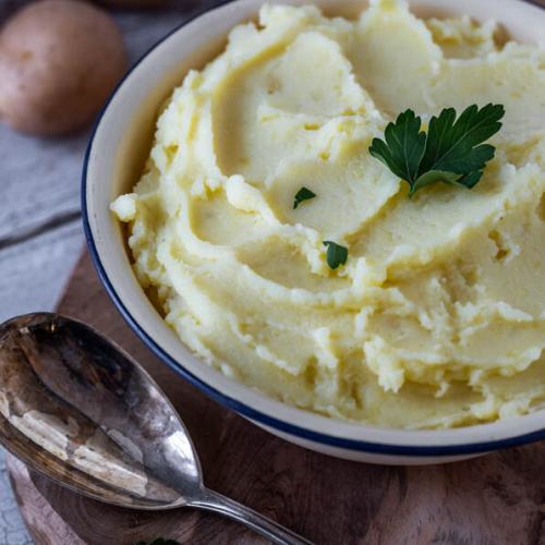 Kartoffelpüree in einer Schale auf einem Holzbrett, daneben ein Löffel