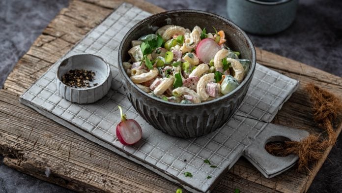 Eine Bowl mit Nudelsalat steht auf einem Bettchen mit Schälchen im Hintergrund