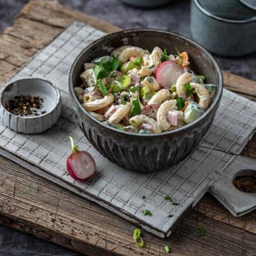 Eine Bowl mit Nudelsalat steht auf einem Bettchen mit Schälchen im Hintergrund