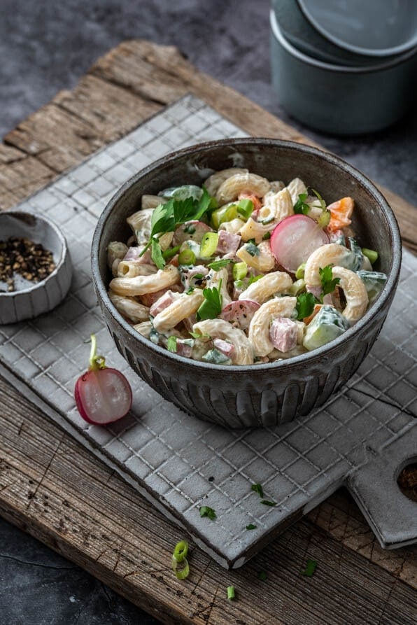 Eine Bowl mit Nudelsalat steht auf einem Bettchen mit Schälchen im Hintergrund