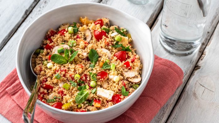 Couscoussalat_Blog_groß_quer_16x9 Kopie Eine Schüssel mit Couscous Salat steht mit einer Wasserflasche und einem Glas auf weißem Holzuntergrund