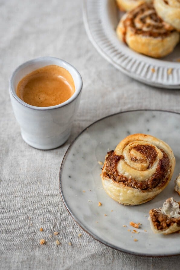 Eine angebissene Nussschnecke auf einem Teller mit einem Espresso.