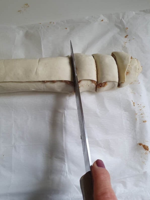 Blätterteigrolle wird mit Messer in Stücke geschnitten.