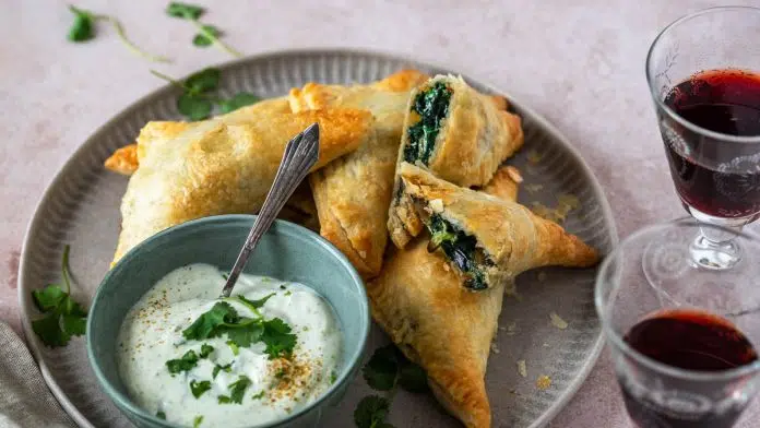 gefuellte-vegane-blaetterteigtaschen-mit-spinat-und-champignons Gefüllte Blätterteigtaschen liegen auf einem Teller und 2 Weingläser stehen daneben