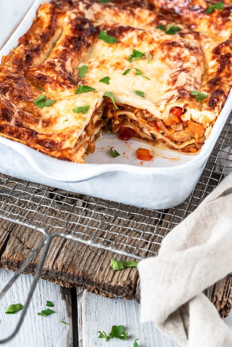 Angeschnittene Gemüselasagne in Auflaufform auf Holzbrett