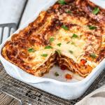 Angeschnittene Gemüselasagne in Auflaufform auf Holzbrett