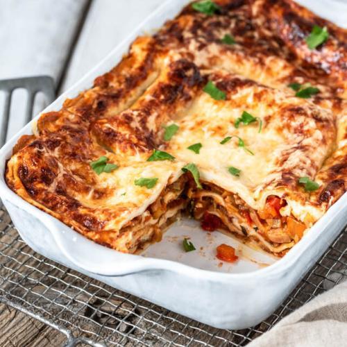 Angeschnittene Gemüselasagne in Auflaufform auf Holzbrett