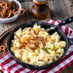 Pfännchen Kässespätzle mit Röstzwiebeln in rustikaler Umgebung