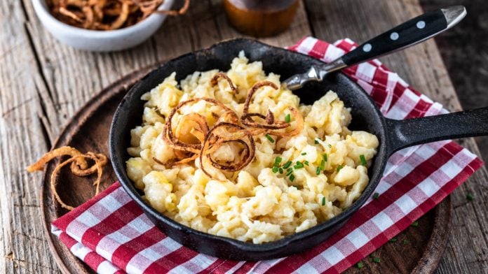 Pfännchen Kässespätzle mit Röstzwiebeln in rustikaler Umgebung