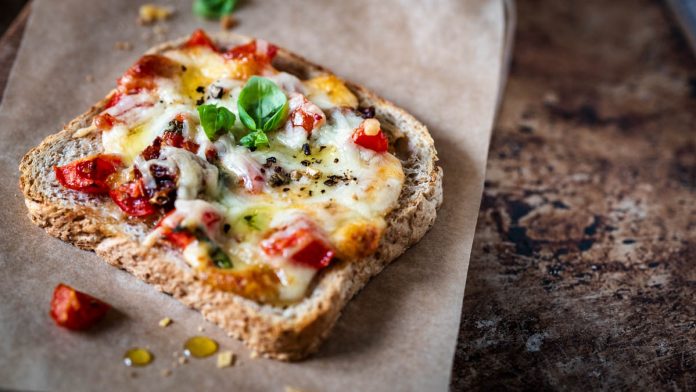 schneller-pizza-toast-vegetarisch Pizza-Toast liegt auf einem Brettchen mit Backpapier und Basilikum