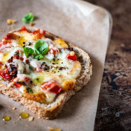 Pizza-Toast liegt auf einem Brettchen mit Backpapier und Basilikum
