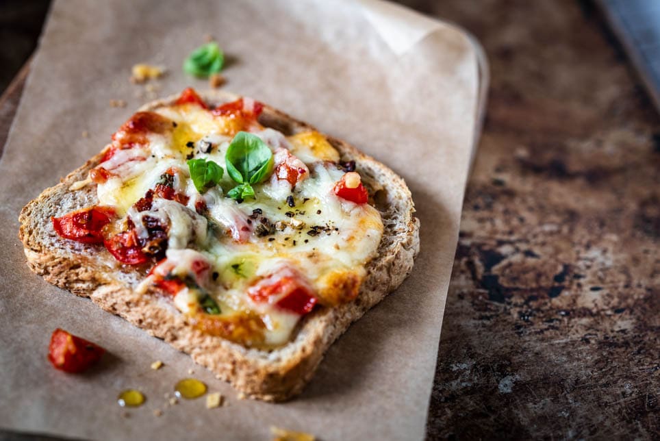 Pizza-Toast liegt auf einem Brettchen mit Backpapier und Basilikum