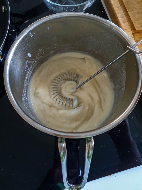 Béchamelsauce mit einem Rührbesen in einem Kochtopf.