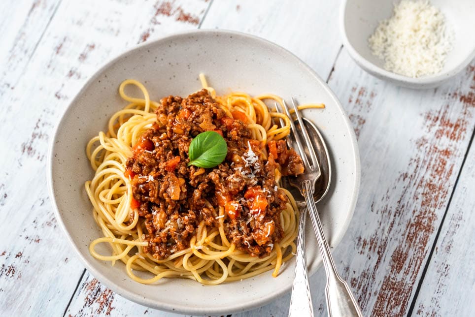 Ein Teller Spaghetti Bolognese mit Besteck und Parmesan