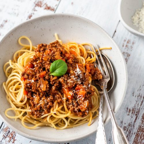 Ein Teller Spaghetti Bolognese mit Besteck und Parmesan