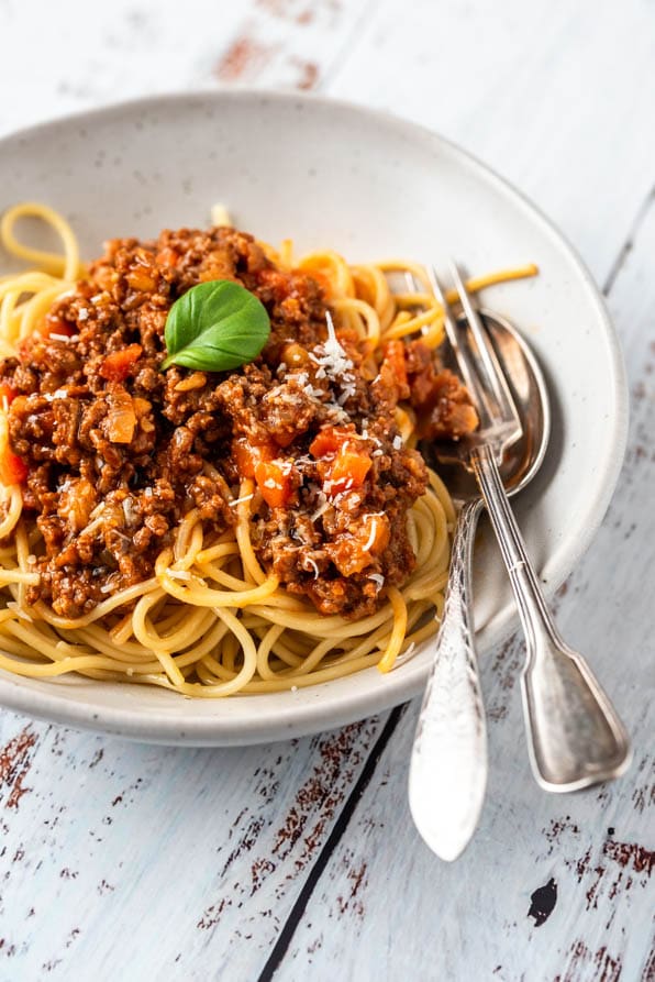 Ein Teller Spaghetti Bolognese mit Besteck und Parmesan