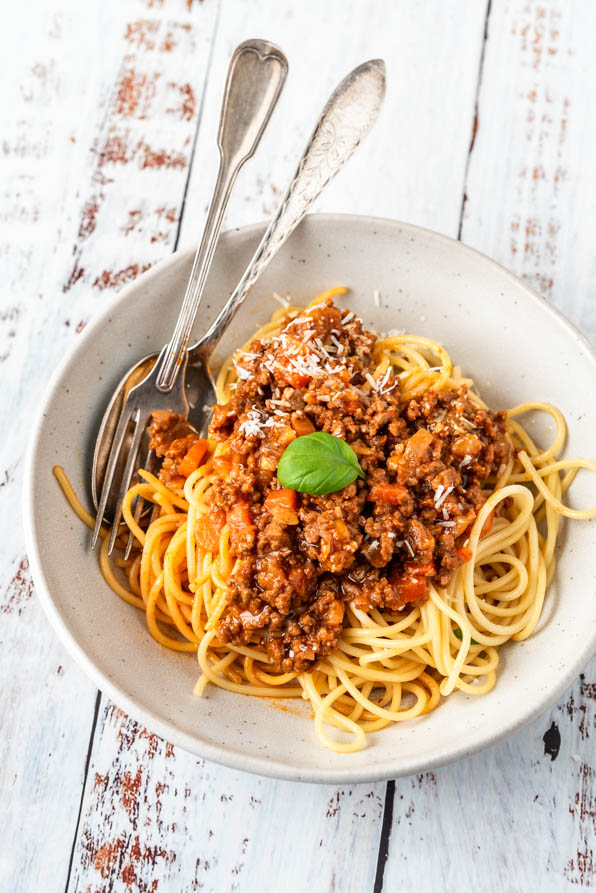 Ein Teller Spaghetti Bolognese mit Besteck und Parmesan