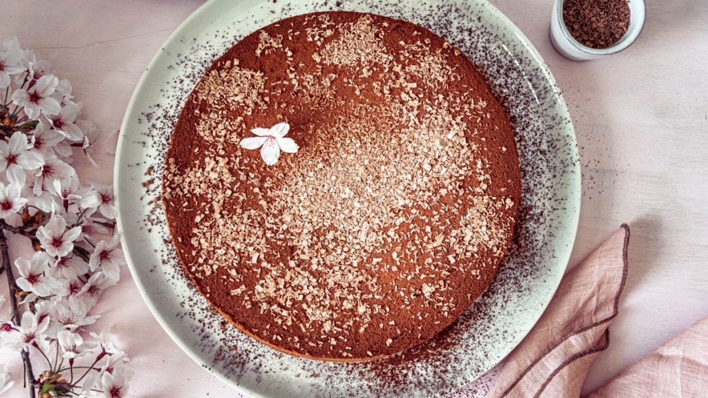 Eine Schokotorte garniert mit Blüten steht auf einem Tortenteller