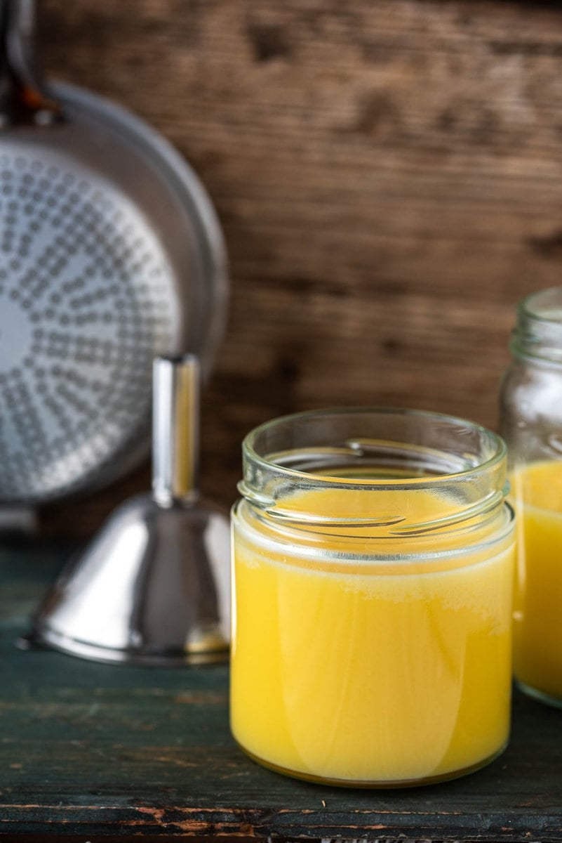 Zwei Gläser Ghee auf Holzuntergrund, dahinter Sieb und Trichter