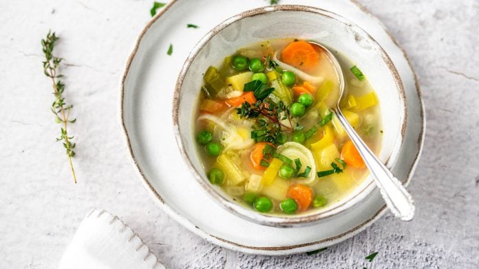 Ein Teller Gemüsesuppe und daneben Kräuter.