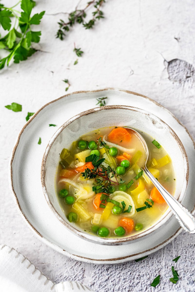 Ein Teller Gemüsesuppe und daneben Kräuter.