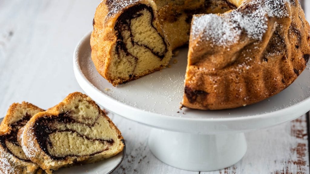 Aufgeschnittener Marmorkuchen auf Etagere und ein Teller davor.
