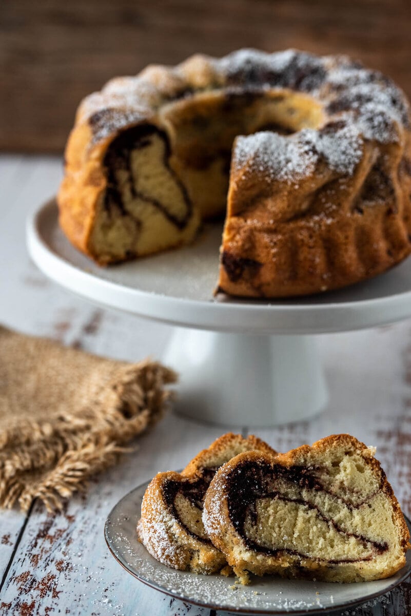Aufgeschnittener Marmorkuchen auf Etagere und ein Teller davor.