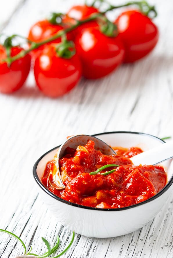 Ein Schälchen mit Tomatensauce und dahinter eine Tomatenrispe