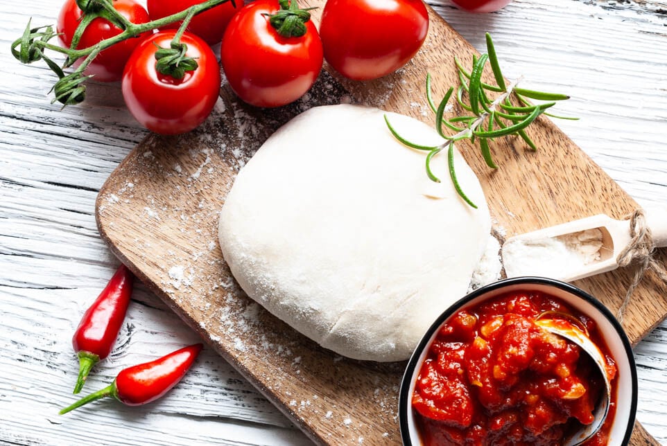 Pizzateig mit Tomaten und Tomatensauce auf Brett