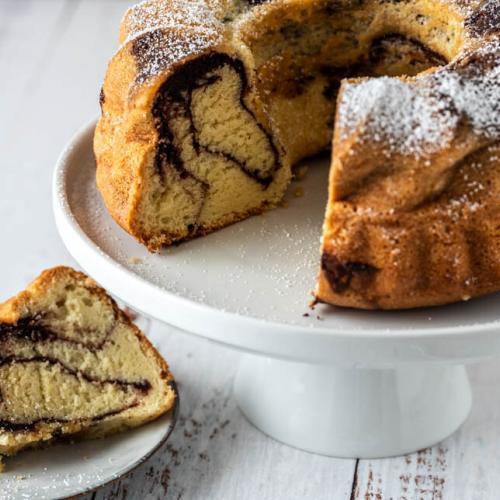 Aufgeschnittener Marmorkuchen auf Etagere und ein Teller davor.