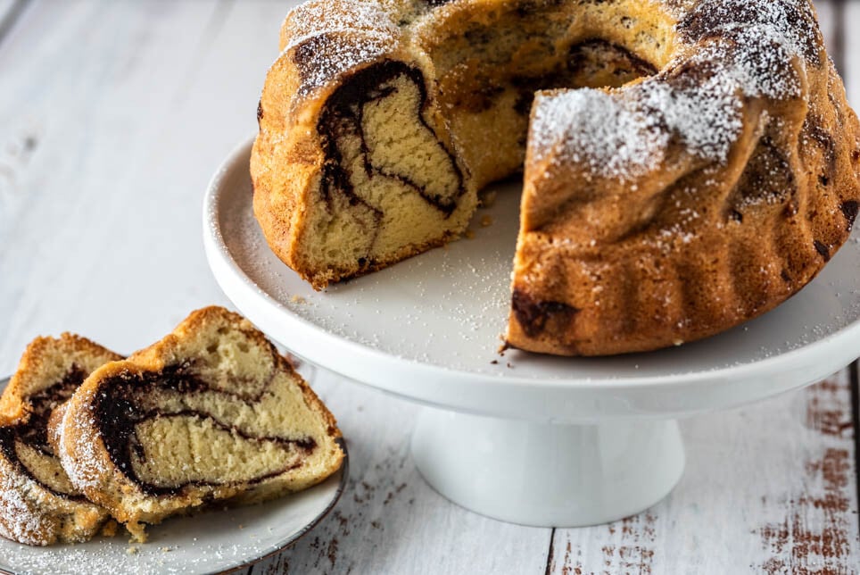 Aufgeschnittener Marmorkuchen auf Etagere und ein Teller davor.