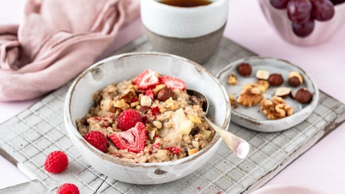 Eine Bowl mit Porridge mit Beeren und Nüssen auf Brett - Mundgefühl