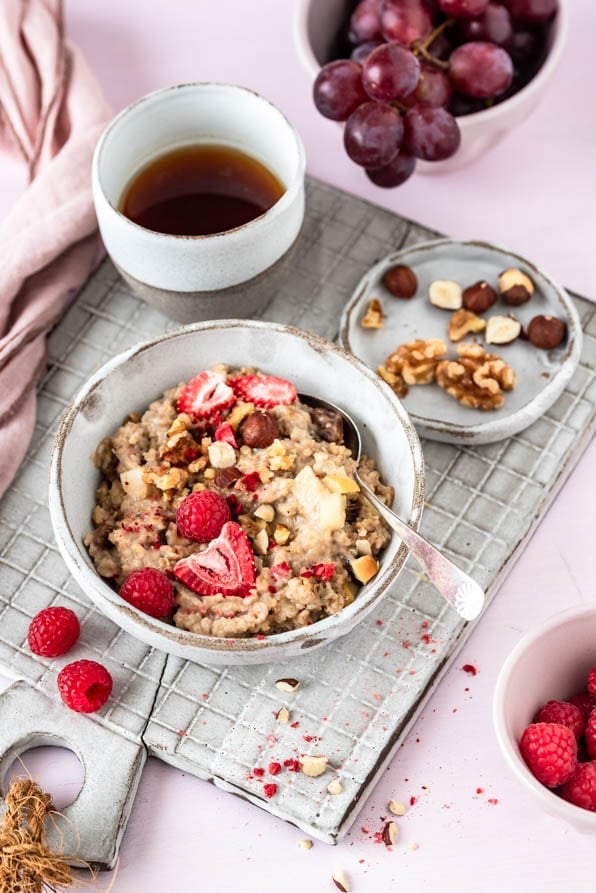 Haferbrei in einer Bowl mit Nüssen und Beeren und einer Tasse Kaffee.